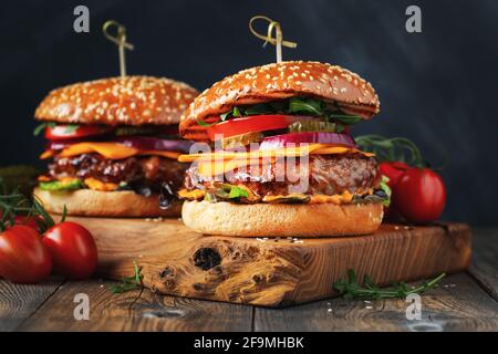 Due deliziosi hamburger fatti in casa di manzo, formaggio e verdure su un vecchio tavolo di legno. Primo piano di alimenti grassi malsani Foto Stock