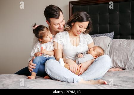 Famiglia multirazziale con due bambini piccoli a letto a. casa Foto Stock