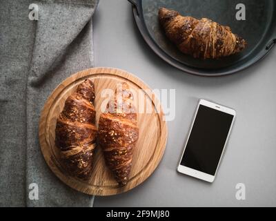 Vista dall'alto di croissant su tavola di legno e schermo per smartphone Foto Stock