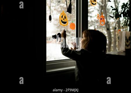 Giovane ragazza che mette Halloween decorazioni su finestre in vita camera Foto Stock