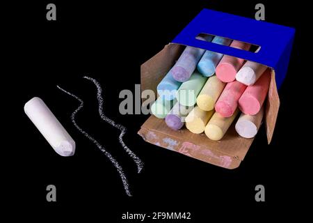 Gesso per disegnare sulla strada in una scatola di cartone. Accessori per giochi creativi per bambini. Sfondo scuro. Foto Stock