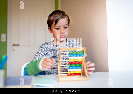 ragazzo freddo con il braccio verde si siede nella sua stanza e impara con la regola di scorrimento con le palle colorate fatte di legno durante homeschooling Foto Stock