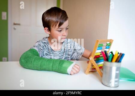 ragazzo freddo con il braccio verde si siede nella sua stanza e impara con la regola di scorrimento con le palle colorate fatte di legno durante homeschooling Foto Stock