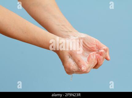 Donna lavando le mani con sapone su sfondo blu. La pulizia corretta delle mani protegge dalle infezioni. Concetto di igiene e pulizia. Foto Stock