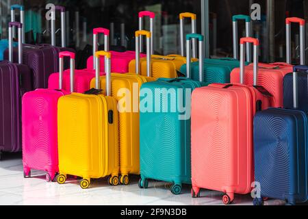 Di fronte al negozio sono in vendita file di valigie blu, rosa e gialle con manici estesi e dimensioni diverse Foto Stock