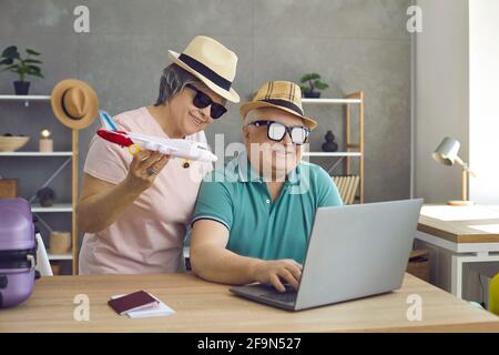 Divertente coppia anziana che pianifica una vacanza utilizzando un computer portatile per prenotare il tour volo Foto Stock