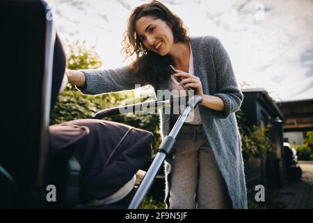 Mamma allegra che spinge un passeggino e guarda il suo bambino. Madre felice con passeggino all'aperto. Foto Stock