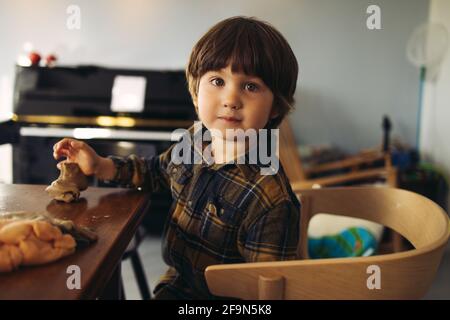 Bambino innocente seduto al tavolo giocando con argilla. Ragazzo carino con argilla di gioco guardando la macchina fotografica. Foto Stock