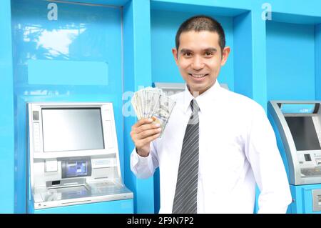 Uomo d'affari asiatico holding money - dollari degli Stati Uniti (USD) - Davanti agli sportelli bancomat Foto Stock