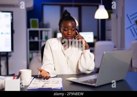 Donna d'affari esausta overworking alla contabilità per la scadenza finanziaria che discute al telefono con il socio circa le statistiche finanziarie. Imprenditore stressato che lavora a tarda notte in ufficio aziendale Foto Stock