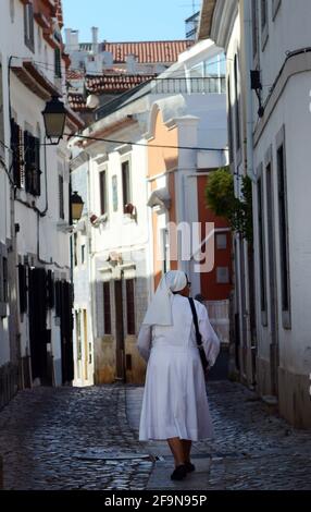 Una suora cattolica che cammina tra i vecchi edifici di Cascais, Portogallo. Foto Stock