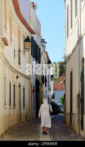 Una suora cattolica che cammina tra i vecchi edifici di Cascais, Portogallo. Foto Stock