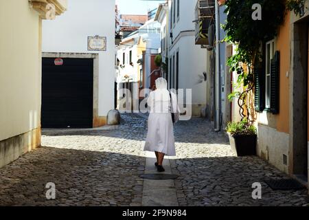 Una suora cattolica che cammina tra i vecchi edifici di Cascais, Portogallo. Foto Stock