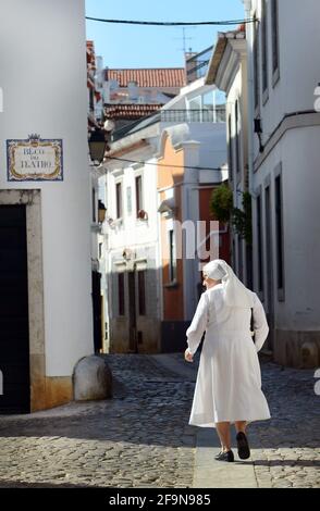 Una suora cattolica che cammina tra i vecchi edifici di Cascais, Portogallo. Foto Stock