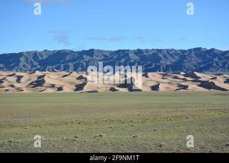 Un paesaggio stratificato di montagne, dune di sabbia e steppa a Khongoryn Els nel Parco Nazionale Gobi Gurvansaikhan, deserto Gobi, Mongolia. Foto Stock