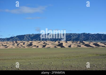 Un paesaggio stratificato di montagne, dune di sabbia e steppa a Khongoryn Els nel Parco Nazionale Gobi Gurvansaikhan, deserto Gobi, Mongolia. Foto Stock