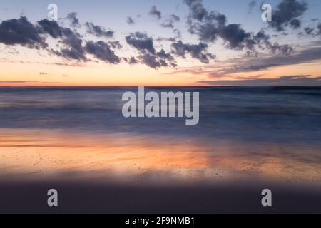 Bel tramonto in spiaggia dopo una giornata estiva, riflessi in acqua Foto Stock