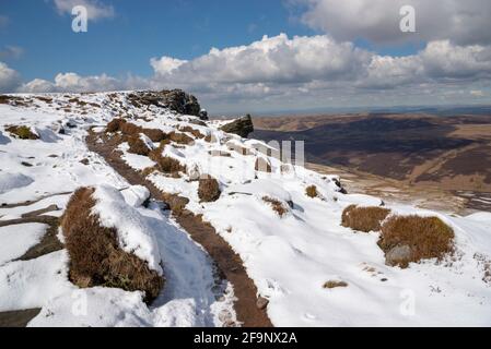 Percorso lungo il bordo settentrionale di Kinder Scout guardando giù sulle brughiere Pennine con insolito mix di neve e sole aprile. Foto Stock