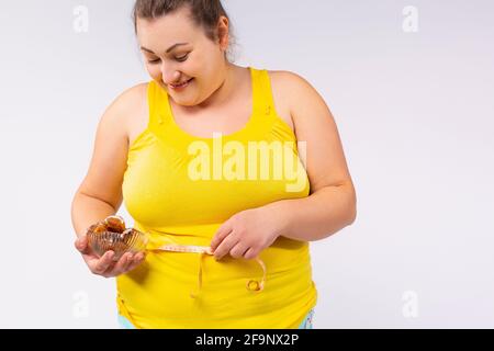 Sono pigro di fare qualcosa e addicted ai dolci. Una donna allegra e piena di bocca, piena di dimensioni, piena di cibo, che tiene un piatto di qualcosa di gustoso Foto Stock