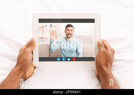 Uomo irriconoscibile sdraiato a letto con tablet digitale, chat video con un amico Foto Stock