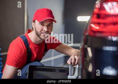 Uomo felice accovacciato lavorando vicino ruota dell'automobile Foto Stock