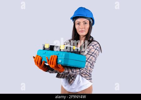 Donna caucasica che guarda serio al toolkit di tenuta della telecamera in officina isolato sfondo grigio. Ingegneria femminile e concetto industriale Foto Stock