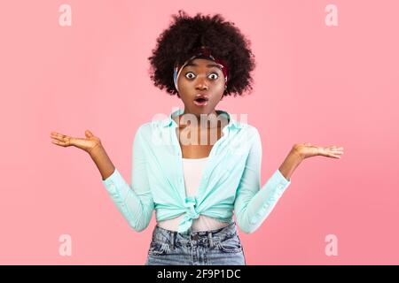 Shocked African American Young Woman Shrugging spalle su sfondo rosa Foto Stock