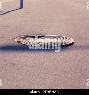 Manhole fognarie danneggiate sul percorso asfaltato, copertura metallica rotta da vicino Foto Stock