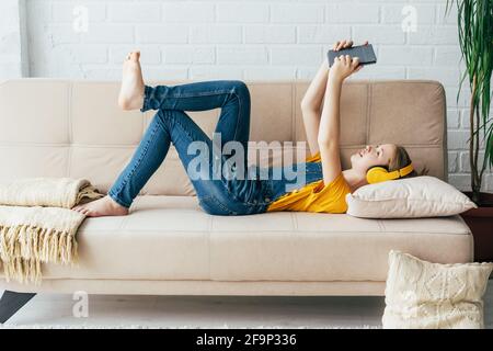 La ragazza adolescente in tute in denim si rilassa nel piacere sul lettino con un tablet elettronico Foto Stock