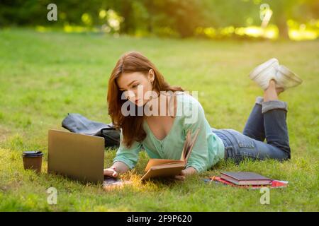 Ragazza della studentessa della scuola superiore di Redhead che si occupa di fare il lavoro con il laptop e. Prenota all'aperto Foto Stock