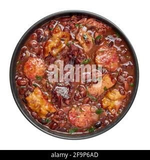 Feijoada in ciotola nera isolata su bianco. Cucina brasiliana e portoghese tradizionale fagioli stufato di carne Foto Stock