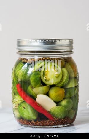 Marinata di barattoli per conserve. In casa rosso scuro sottaceti pomodori  con basilico, prezzemolo fresco, aneto, spezie d'estate all'aperto.  Alimento fermentato Foto stock - Alamy