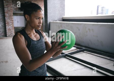 Determined FIT donna afroamericana che esercita tenendo palla da pallavolo in spazio vuoto magazzino. Fitness urbano e sport. Foto Stock