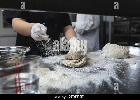 Sezione centrale di pasta per impastare da chef professionisti con guanti sanitari. Lavoro in una cucina del ristorante molto affollata. Foto Stock