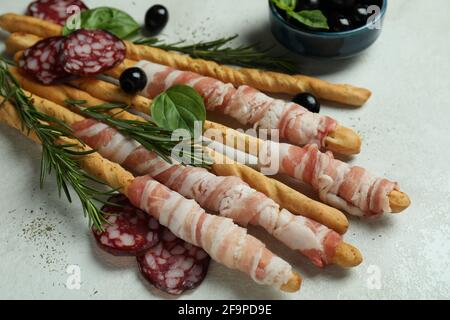 Bastoncini di grissini con pancetta e spuntini su fondo testurizzato bianco Foto Stock