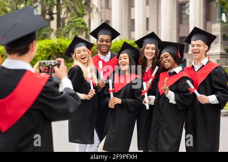 Positivi studenti internazionali che festeggiano la laurea, scattano foto Foto Stock