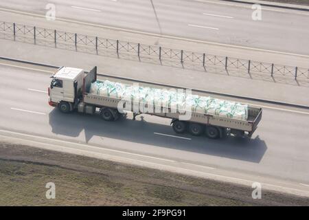 Autocarro pesante con rimorchio e carico sfusi in sacchi- zolfo industriale, sostanze chimiche, veleni, merci pericolose che corre sull'autostrada in città Foto Stock