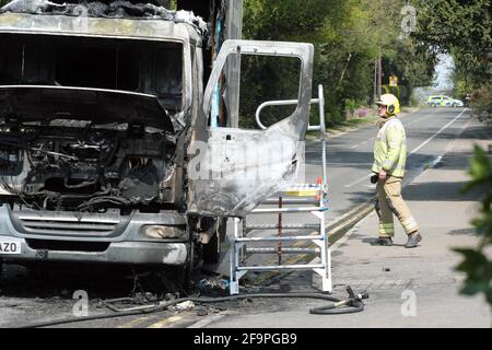 Hereford, Herefordshire Regno Unito - Martedì 20 aprile 2021 - UN vigile del fuoco ispeziona il relitto del camion di consegna del latte bruciato che ha preso fuoco sulla collina occupata di Aylestone nel nord della città di Hereford oggi a pranzo. Il camion del latte appartiene al locale Bartonsham Farm Dairy di Hereford. Photo Steven May / Alamy Live News Foto Stock