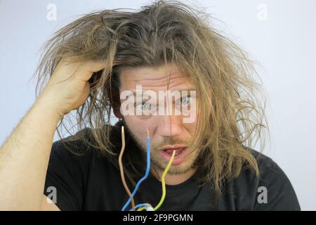 Divertente uomo serbo che tiene un cavo elettrico dopo aver ottenuto un scossa elettrica a casa Foto Stock