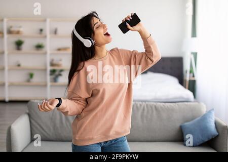 Giovane donna che canta usando lo smartphone come microfono Foto Stock