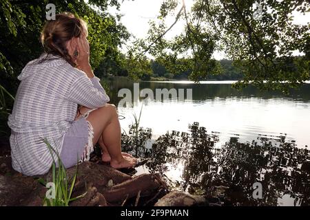 07.09.2018, Walkmuehle, Brandeburgo, Germania - Silhouette, donna che si siede a lungo sulla riva di un lago. 00S180907D427CAROEX.JPG [VERSIONE DEL MODELLO: SÌ Foto Stock