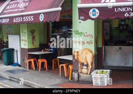 10.03.2021, Singapore, , Singapore - UN uomo si siede bevendo una tazza di tè nell'area esterna di un ristorante indiano nel quartiere di Little India dur Foto Stock