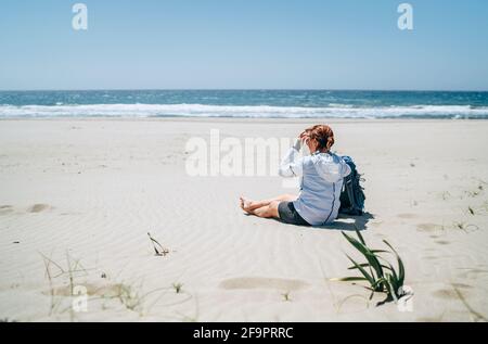 Backpacker donna seduta sulla spiaggia di sabbia di Patara godendo il ventoso Mar Mediterraneo durante la passeggiata di trekking Lycian Way. Famoso Likya Yolu Turki Foto Stock