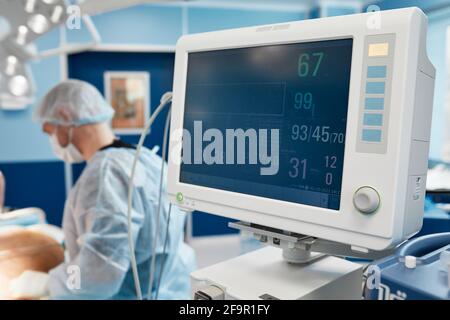 Anestesista che tiene traccia delle funzioni vitali del corpo durante la chirurgia cardiaca. Chirurgo che guarda il monitor medico durante l'intervento chirurgico. Dottore scacchi Foto Stock