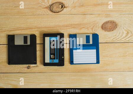 Su uno sfondo di legno con nodi è una cassetta audio e due floppy disk. Uno è blu, l'altro è nero. Vista dall'alto Foto Stock