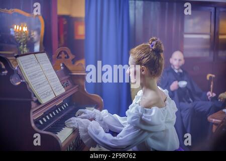 LUKOVICA, SLOVENIA - 03 aprile 2017: Giovane coppia in soggiorno d'epoca, donna suona piano, l'uomo ama la sua performance Foto Stock