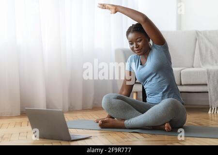 Fitness online. Corso di formazione Smiling Black Lady davanti al laptop a casa Foto Stock