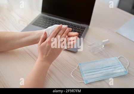 Donna che disinfetta le mani durante la pandemia di covid-19 dopo l'uso di gadget, lavorando a casa. Foto Stock