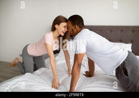 Bella coppia multirazziale divertirsi a letto a casa, toccando le fronte, guardarsi l'un l'altro con amore Foto Stock