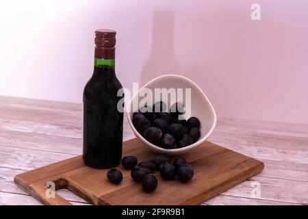 Uva rossa posta in una ciotola di porcellana e su un tagliere di legno insieme ad una bottiglia di vino rosso della Spagna che crea un'ombra sul muro. Foto Stock